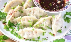 Ugotowane pierożki gyoza posypane szczypiorkiem, sezamem i papryką, podane z sosem.