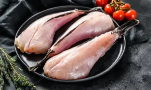 Trzy filety z ryby diabeł morski na czarnym talerzu, obok gałązka tymianku i pomidorki koktajlowe.