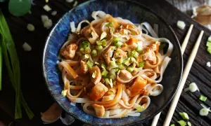 Miseczka makaronu ryżowego z kurczakiem, posypana szczypiorkiem i orzechami, w sosie Pad Thai.