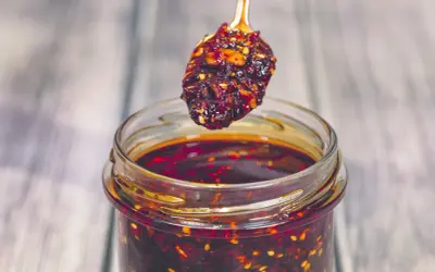 Łyżeczka z aromatycznym chili w oleju nad słoikiem pełnym tej pikantnej przyprawy.