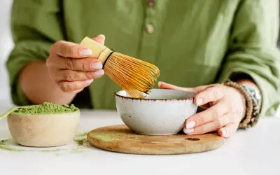 Przygotowanie najlepszej zielonej herbaty matcha. W rękach bambusowa miotełka do spieniania, obok miseczka z zielonym proszkiem.