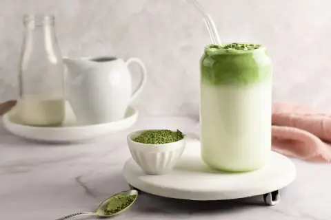 Orzeźwiające matcha z mlekiem kokosowym, z proszkiem matcha na łyżeczce i w miseczce.