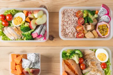 Cztery pojemniki z kolorowymi, zdrowymi posiłkami typu bentos: kurczak, ryż, warzywa i owoce.