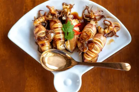 Smażone kalmary mrożone w sosie, ozdobione kolendrą i papryczką chili, na białym talerzu z łyżką.
