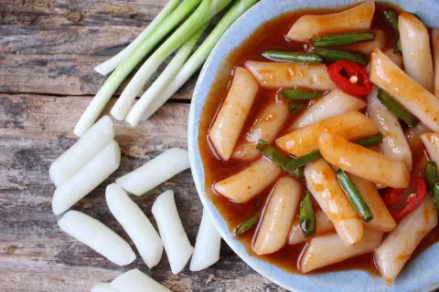 Pyszne kluski ryżowe tteokbokki w pikantnym sosie, podane z dymką i papryczką chili.
