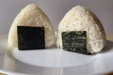 Dwa japońskie kulki ryżowe, onigiri, z kawałkami nori na białym talerzu.