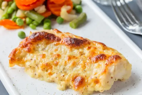 Pyszny, zapieczony filet z dorsza w sosie serowym, podany z kolorowymi warzywami.