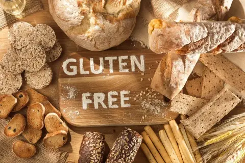 Różnorodne pieczywo i przekąski, na desce napis "GLUTEN FREE". Dowiedz się, co to jest gluten i jak go unikać.