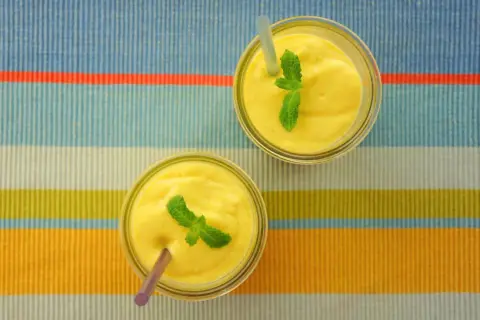 Dwa pyszne mango lassi, orzeźwiające napoje z Indii, ozdobione listkami mięty, czekają na spróbowanie.
