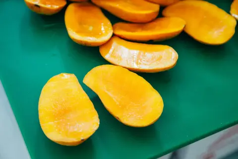 Pokrojone w łódeczki, soczyste mango w ciąży, gotowe do jedzenia, leżą na zielonej desce.