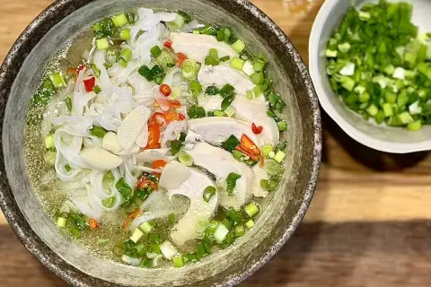 Aromatyczna zupa pho ga z kawałkami kurczaka, makaronem ryżowym, szczypiorkiem i papryczką chili. Obok miseczka z posiekanym szczypiorkiem.
