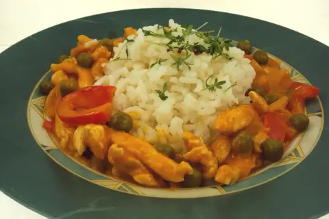 Pyszne tajskie curry z kurczakiem, podane z ryżem i zielonym groszkiem. Danie ozdobione jest świeżymi ziołami.