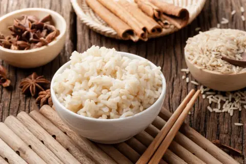 Miseczka parującego congee, obok miseczki z ryżem, anyżem i laskami cynamonu.