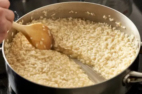 Gotuje się kremowy ryż do risotto w garnku, mieszany drewnianą łyżką.