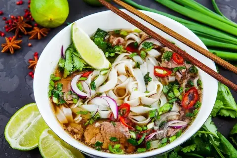 Aromaticzny makaron pho z wołowiną, świeżą kolendrą, cebulą i chili. Podany z limonką i pałeczkami.