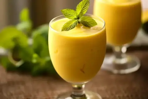 Gęsty, kremowy mango lassi w kieliszku, ozdobiony listkami mięty. Idealny na orzeźwienie.