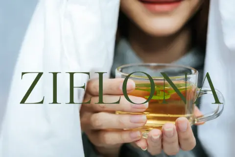Kobieta otulona kocem trzyma kubek z zieloną herbatą. Idealny napój na czczo dla odprężenia i dobrego samopoczucia.