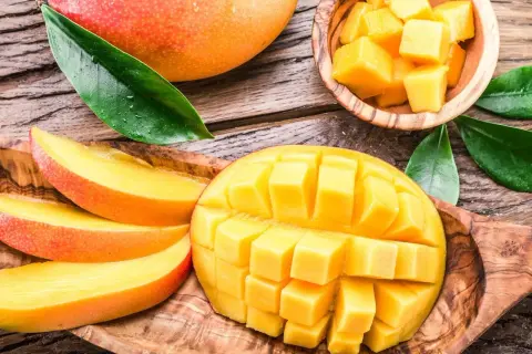 Soczyste, pokrojone w kostkę i plastry mango, które pokazuje, co to jest mango. Całe, dojrzałe owoce i liście na drewnianym tle.
