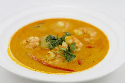 Aromatyczna zupa tom yum z krewetkami, ozdobiona świeżą kolendrą i kawałkami chili, podana w białej misce.