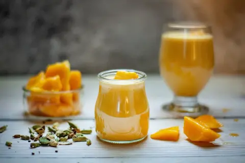 Słodki jogurt z mango, udekorowany kawałkami owoców, obok miseczki z mango i kardamonu.