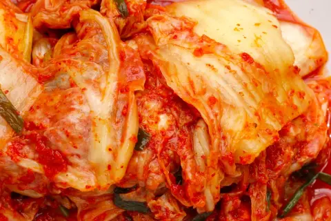 Pikantna kapusta kimchi, z widocznymi liśćmi i przyprawami, gotowa do podania.