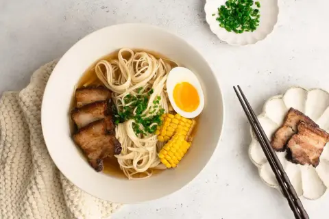 A miseczce shoyu ramen z makaronem, plastrami boczku, jajkiem na pół, kukurydzą i szczypiorkiem.