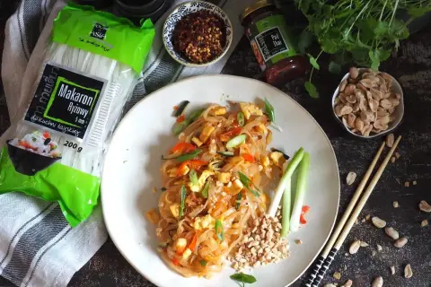 Pyszny pad thai z wołowiną, makaronem ryżowym i orzeszkami ziemnymi. Obok składniki: makaron, sos i płatki chili.