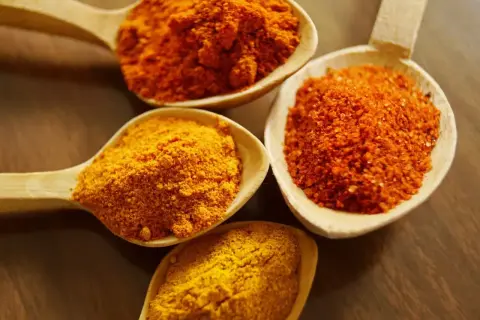 Drewniane łyżki wypełnione przyprawami: intensywnie żółta kurkuma i pomarańczowe proszki, idealne do aromatycznego curry.