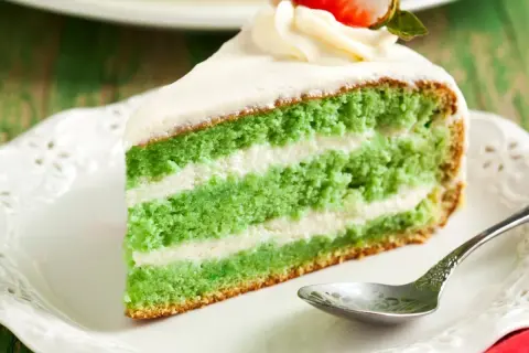 Zielone ciasto z matcha i mascarpone, przełożone kremem, ozdobione bitą śmietaną i truskawką.