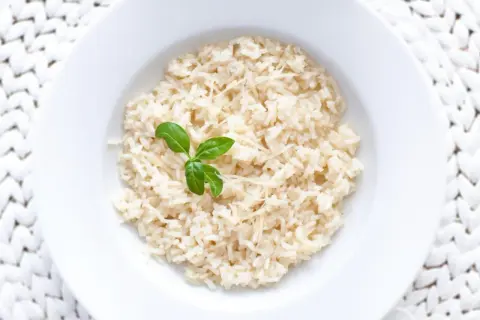 Ryż parboiled co to? Gotowany ryż z parmezanem i listkiem bazylii na białym talerzu.