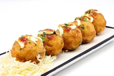 Pięć złotych kulek takoyaki, polanych majonezem i sosem, na białym talerzu z poszatkowaną kapustą. Idealne japońskie przekąski, przepisy na nie są proste!