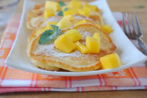 Puszyste placuszki z cukrem pudrem i kostkami mango, ozdobione listkami mięty. Idealne śniadanie z mango.