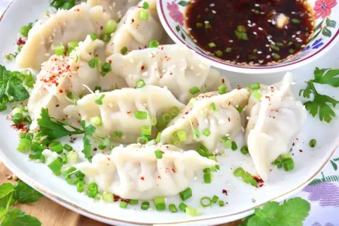 Ugotowane pierożki gyoza posypane szczypiorkiem, sezamem i papryką, podane z sosem.