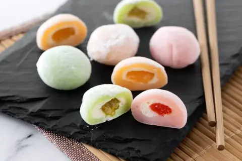 Kolorowe mochi z owocowym nadzieniem, idealne do domowego przepisu na mochi. Patyczki do jedzenia obok.