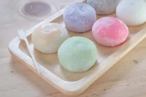 Kolorowe japońskie lody mochi na drewnianej tacy, wyglądają jak małe, słodkie kuleczki.