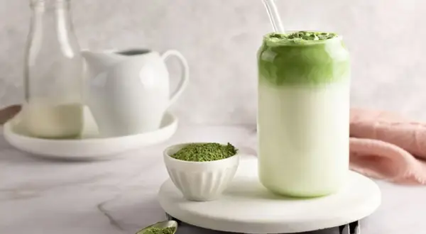 Orzeźwiające matcha z mlekiem kokosowym, z proszkiem matcha na łyżeczce i w miseczce.