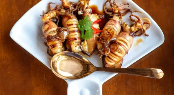 Smażone kalmary mrożone w sosie, ozdobione kolendrą i papryczką chili, na białym talerzu z łyżką.