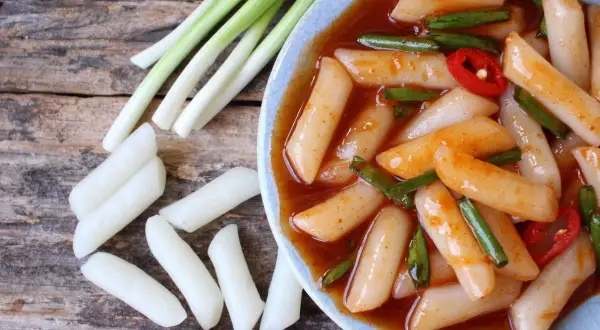Pyszne kluski ryżowe tteokbokki w pikantnym sosie, podane z dymką i papryczką chili.