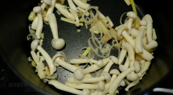 Grzybki shimeji smażą się na patelni z cebulką i imbirem, tworząc aromatyczne danie.