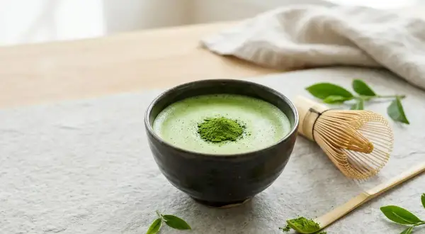 Aksamitna, zielona matcha w ceramicznej miseczce, obok bambusowa miotełka i łyżeczka. Poczuj, jak smakuje matcha.