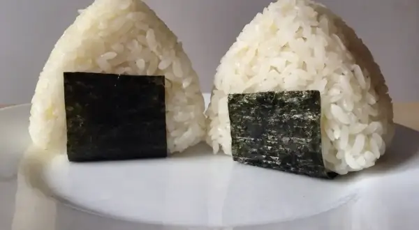 Dwa japońskie kulki ryżowe, onigiri, z kawałkami nori na białym talerzu.