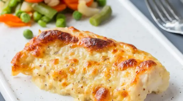 Pyszny, zapieczony filet z dorsza w sosie serowym, podany z kolorowymi warzywami.