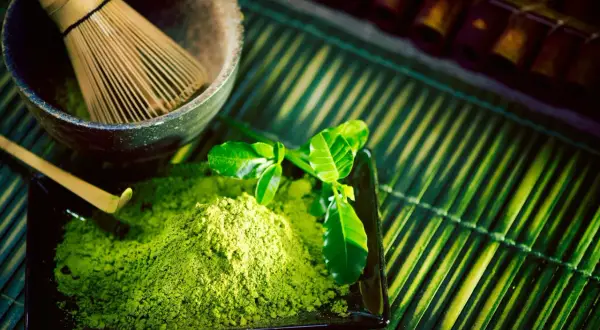 Zielony proszek matcha na czarnym talerzyku, bambusowa miotełka i liście.