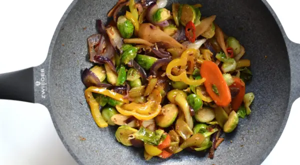 Kolorowe warzywa stir fry z brukselką, papryką i marchewką na patelni.
