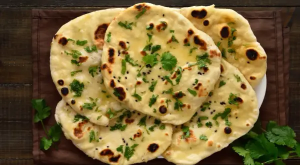 Stos chlebków naan, posypanych kolendrą i czarnuszką, z widocznymi pęcherzykami powietrza. Idealne do curry, ale warto sprawdzić chlebek naan kcal.