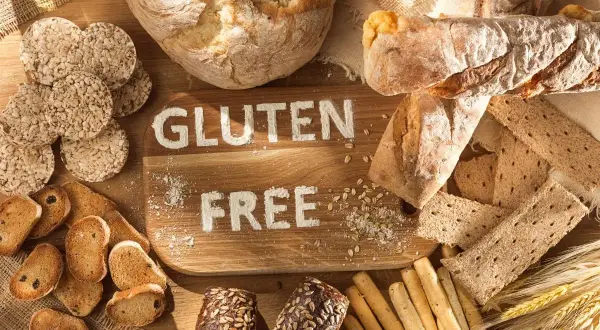 Różnorodne pieczywo i przekąski, na desce napis "GLUTEN FREE". Dowiedz się, co to jest gluten i jak go unikać.