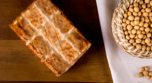 Wędzone tofu z kratką na drewnianym tle, obok koszyczek z ziarnami soi. Idealne do zdrowych posiłków, niskokaloryczne.