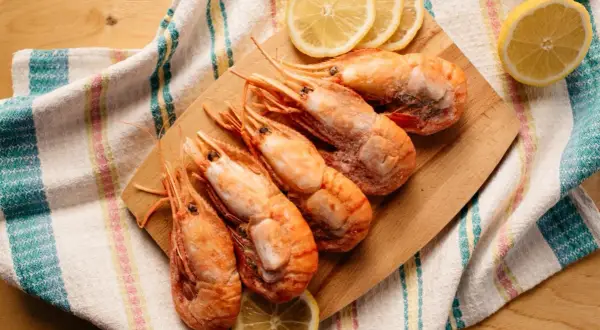 Jak jeść krewetki w restauracji? Na drewnianej desce leżą krewetki z cytryną, obok kolorowy ręcznik.