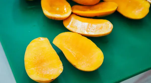 Pokrojone w łódeczki, soczyste mango w ciąży, gotowe do jedzenia, leżą na zielonej desce.