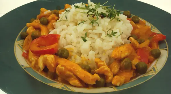 Pyszne tajskie curry z kurczakiem, podane z ryżem i zielonym groszkiem. Danie ozdobione jest świeżymi ziołami.
